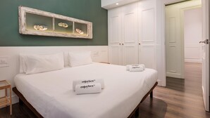 A neatly made bed with white linens and two towels with "enjoyben" text, a wall-mounted mirror with shoes, and a white wardrobe. - Design and comfort on the Rambla (Barcelona)