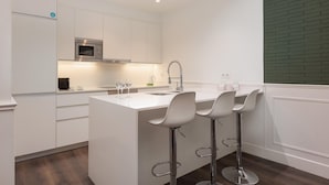 A modern kitchen with white cabinetry, a central island with bar stools, a stainless steel microwave, and a green brick accent wall. - Design and comfort on the Rambla (Barcelona)