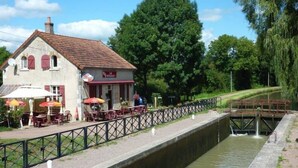 Un restaurant doté d’une terrasse donnant sur un canal, avec une écluse et une végétation luxuriante.