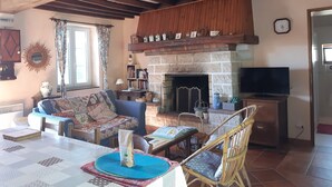 Un salon chaleureux avec une cheminée, des poutres apparentes, un canapé, une table avec un set de table et un téléviseur.