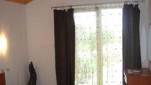 Un dormitorio con cama, techo de madera, escritorio con silla, ventana con cortinas y un taburete pequeño.