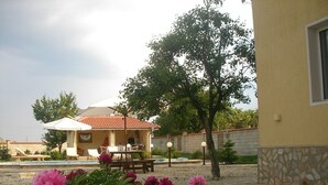 Una villa con patio, mobiliario exterior y un jardín lleno de flores rosadas.
