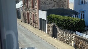 A stone building with a red roof and a white window, located on a street with a car parked in front.