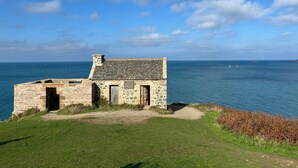 A stone building with a sloped roof overlooking a body of water.