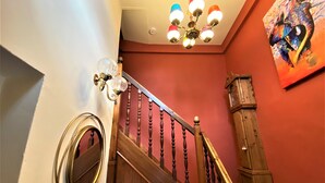 Eine Treppe mit Holzspindeln und Handlauf, ein an der Wand befestigter Spiegel und eine Deckenleuchte.