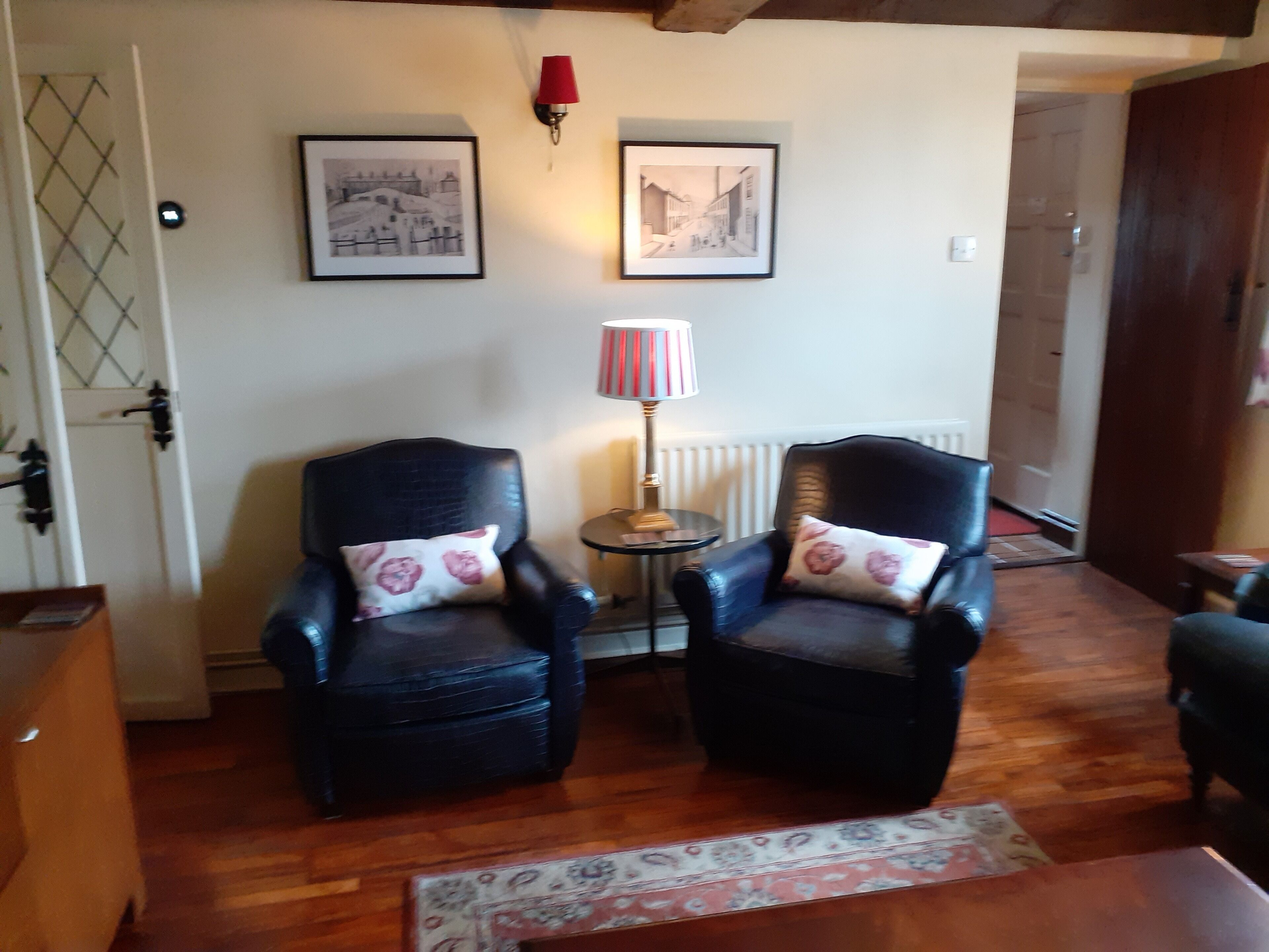 Une pièce comprenant deux fauteuils en cuir noir, une petite table ronde, un lampadaire et deux tableaux encadrés accrochés au mur.