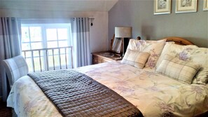 Une chambre d’hôtel avec un lit, une chaise, une table de chevet, une lampe et une fenêtre avec des rideaux.