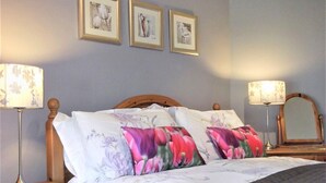 Ein ordentlich bezogenes Bett mit floralen Kissen, zwei Nachttischlampen und drei gerahmte Bilder an der Wand.