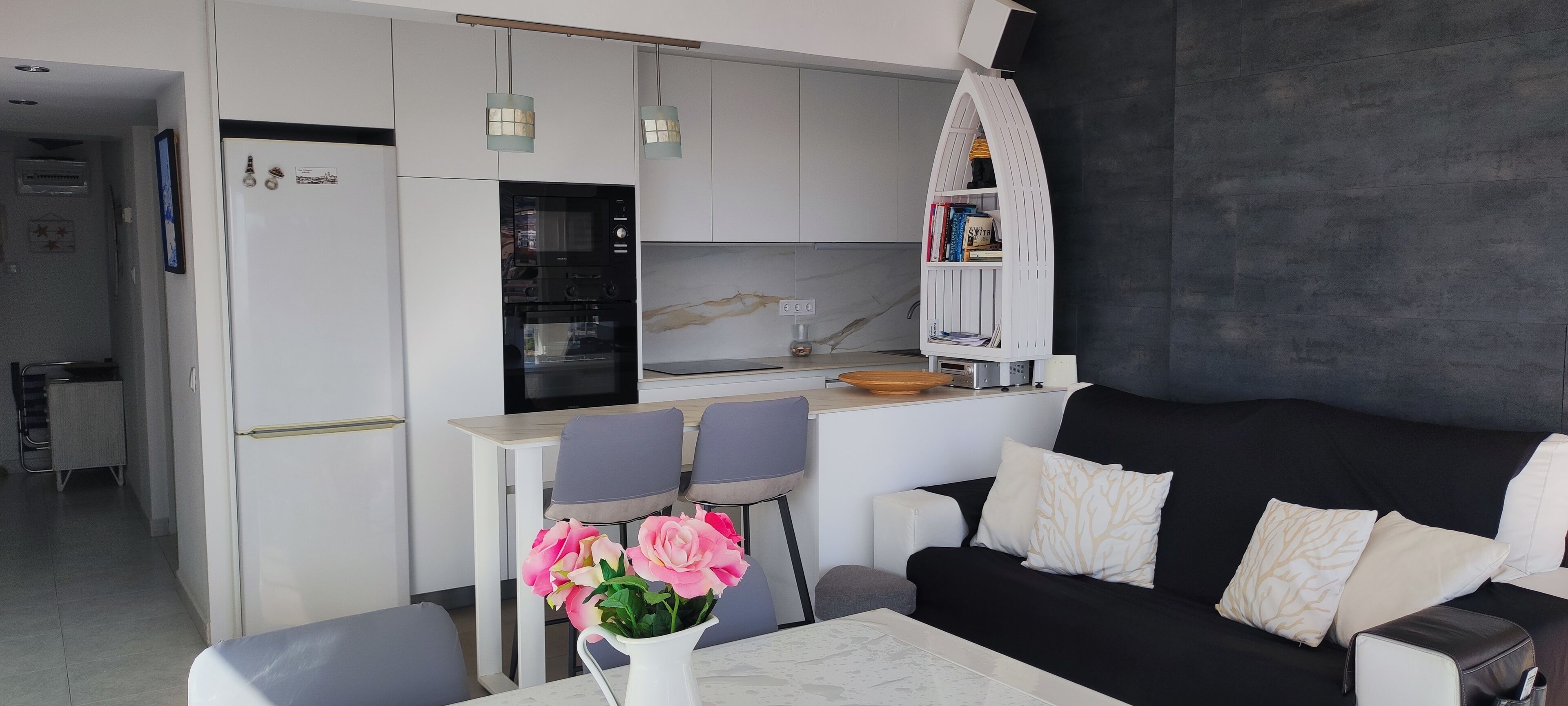 Une cuisine moderne avec des armoires blanches, un four encastré et un coin repas comprenant deux chaises et une table.