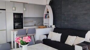 A modern kitchen with white cabinets, a built-in oven, and a dining area with two chairs and a table. - Sitges: Apartment/ flat - SITGES (Sitges)