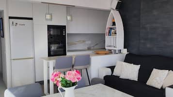 Une cuisine moderne avec des armoires blanches, un four encastré et un coin repas comprenant deux chaises et une table.
