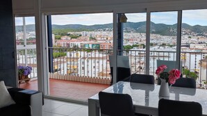 A balcony with a table and chairs, overlooking a cityscape with buildings and hills. - Sitges: Apartment/ flat - SITGES (Sitges)