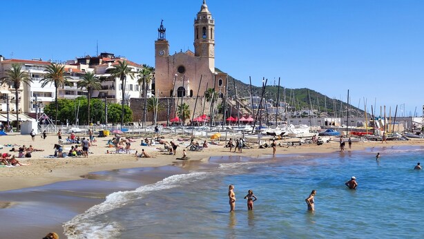 A beach with a prominent church tower, a marina with boats, and people enjoying the seaside. - Sitges: Apartment/ flat - SITGES (Sitges)