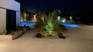 Ein moderner Poolbereich im Freien mit einer Steinmauer und Palmen, umgeben von einer gut beleuchteten Terrasse.