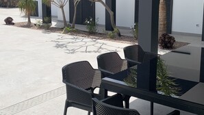 Ein Außenbereich mit Sitzgelegenheiten, Tisch und Stühlen, umgeben von Pflanzen und einer modernen Gebäudefassade.