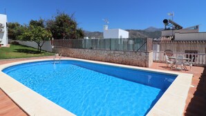 En pool med en mur av sten, en uteplats med utemöbler och en utsikt över berg i bakgrunden.