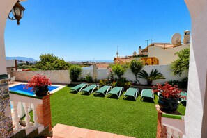 A poolside area with green lounge chairs, a small pool, and a view of the sea and buildings in the distance. - 1022 Villa Jorge (Nerja)