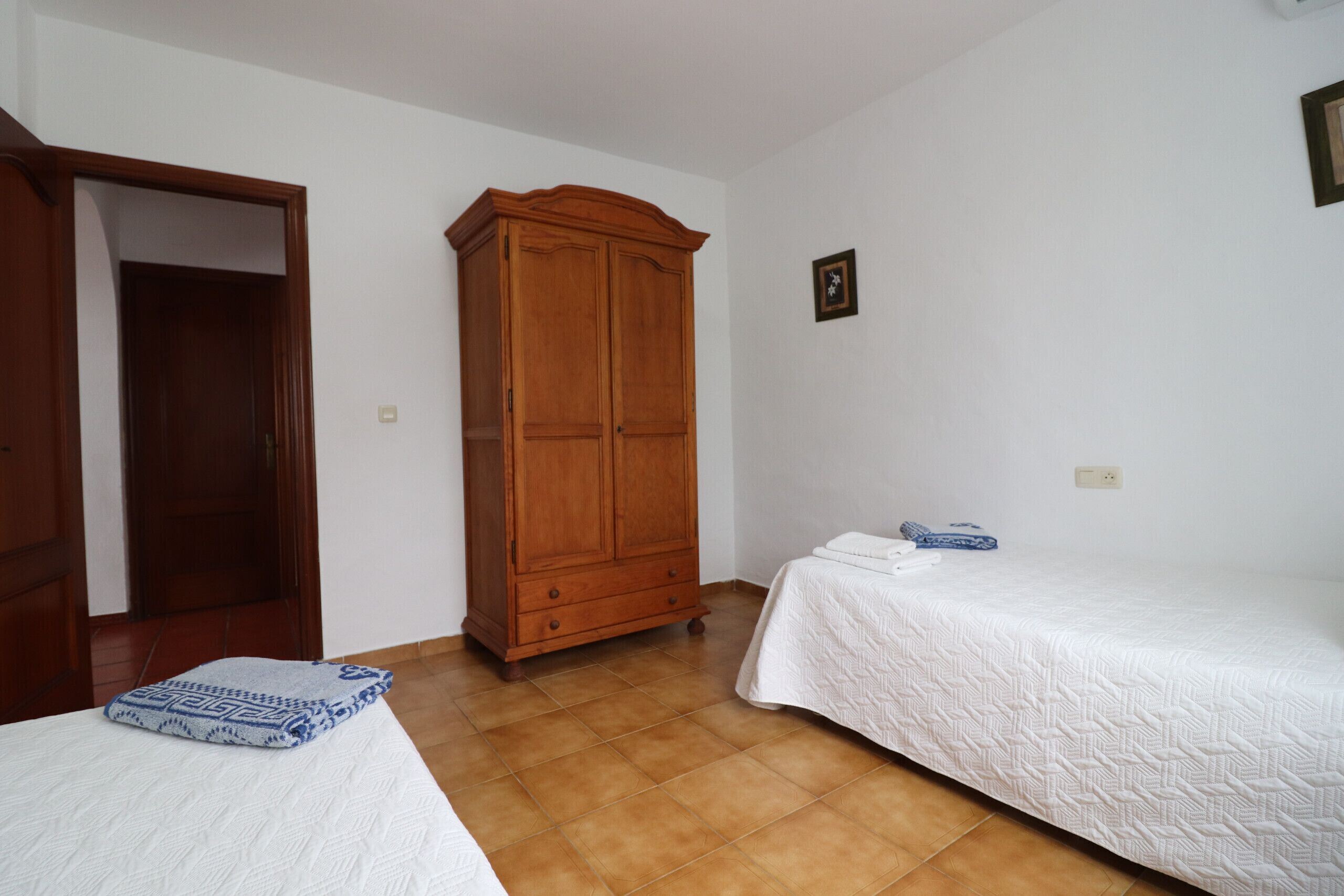 Una camera da letto con due letti singoli, un armadio in legno e una porta che dà su un'altra stanza.
