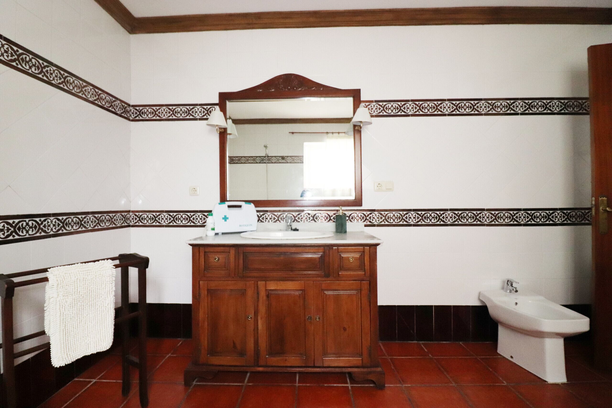 A bathroom with a wooden vanity, a mirror, a bidet, and a towel rack.