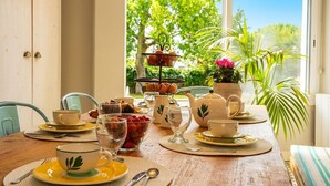 A dining table set with tea cups, a teapot, a fruit bowl, and a tiered fruit stand.