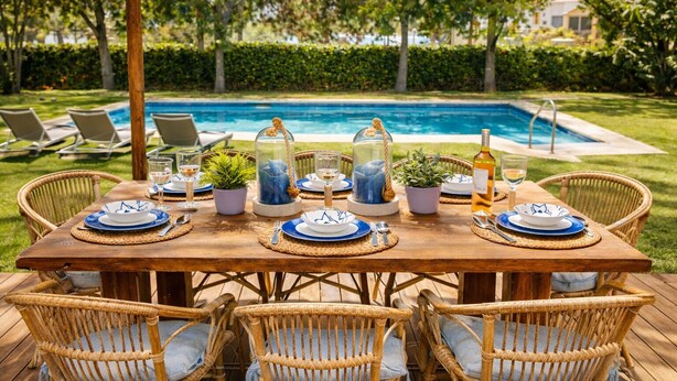 An outdoor dining setup with a pool view, wicker chairs, and a wooden table.