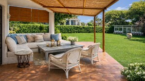A covered patio with a sofa, table, and wicker chairs.