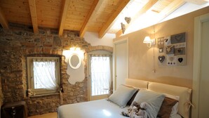 Ein Schlafzimmer mit Steinwand, Holzbalken, einem Bett mit Kissen, einem Teddybären, einem Spiegel und Wanddekorationen.