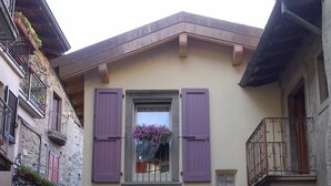 Ein zweigeschossiges Gebäude mit einer Stein-Fassade, einem Balkon mit schmiedeeisernen Geländern und einem Fenster mit violetten Rollläden.