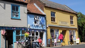 Une scène de rue avec un bâtiment portant l’inscription « JOULES » et un autre avec une enseigne indiquant « The Burnhams Tea Room & Cafe ».