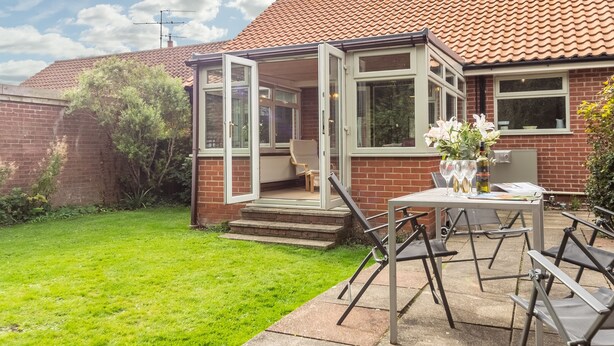 Une maison dotée d’un patio, d’une porte vitrée donnant sur un espace extérieur aménagé pour se détendre, et d’une façade en briques.