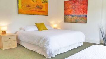 A bedroom with a large bed, two bedside tables with lamps, and two abstract paintings on the walls.