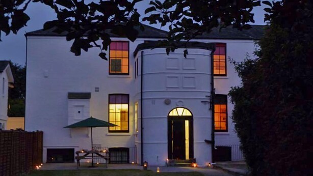 A white building with a curved facade, a central arched entrance, and multiple windows with warm lighting.