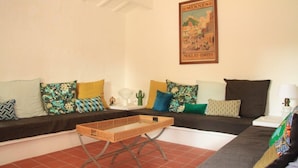 A living room with a sofa set, a wicker coffee table, and a wall-mounted poster. - Charming house in the old part of Sant Lluis, near the mill (Sant Lluís)