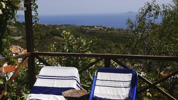 Une terrasse dotée de deux chaises longues, l’une recouverte d’une housse bleue et l’autre d’une housse blanche, offrant une vue sur un paysage côtier.
