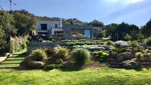 Una casa moderna con fachada de piedra, rodeada por un jardín cuidado con diversas plantas y rocas.