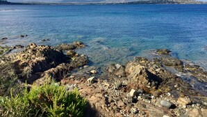 Una costa rocosa con aguas azul turquesa y montañas a lo lejos.