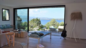 Una sala de estar moderna con un gran ventanal que da a un balcón con vistas al mar.