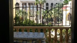 A balcony with a table and chairs, a view of a building with a crown emblem, and a fenced garden area.