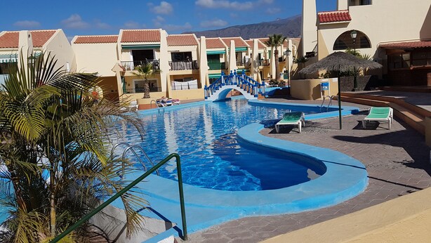 A resort pool area with a curved pool, lounge chairs, and a staircase leading to a balcony.