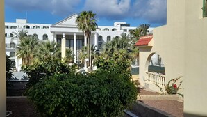 A courtyard with a large bush, a building with columns, and a red-roofed structure.