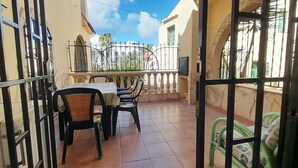 A balcony with a table and chairs, a tiled floor, and a view of a building with a fence.