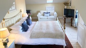 A bedroom with a bed, a white sofa, a television, and a small table.
