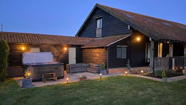A two-story house with a patio area featuring a hot tub, seating, and potted plants.