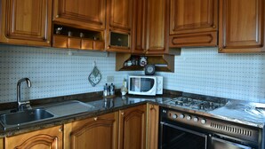 A kitchen with wooden cabinets, a stainless steel sink, a microwave, and a gas stove. - Sagui apartment in the heart of the Dolomites CIN 025069C2H8ECUEQQ  (Zoppe' di Cadore (Belluno))
