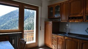A kitchen with wooden cabinets, a sink, and a window overlooking a forested mountain. - Sagui apartment in the heart of the Dolomites CIN 025069C2H8ECUEQQ  (Zoppe' di Cadore (Belluno))
