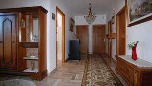 A hallway with wooden doors, a chandelier, a patterned rug, and a red vase on a console table. - Sagui apartment in the heart of the Dolomites CIN 025069C2H8ECUEQQ  (Zoppe' di Cadore (Belluno))