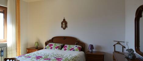 Een slaapkamer met een bed, houten nachtkastjes, een dressoir, een stoel, een spiegel en een wandklok.