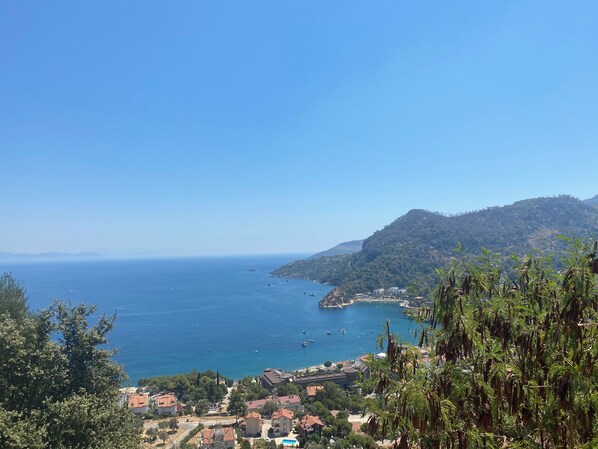 A coastal town with buildings near the sea, a clear sky, and a hilly landscape.