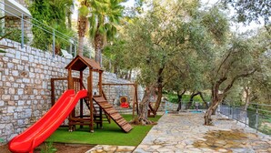 Un parque infantil con un tobogán rojo, estructuras de madera para escalar y una casita de madera.