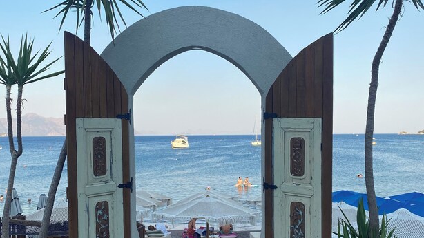 Una entrada a la playa con un arco de madera, plantas en macetas y asientos al aire libre.